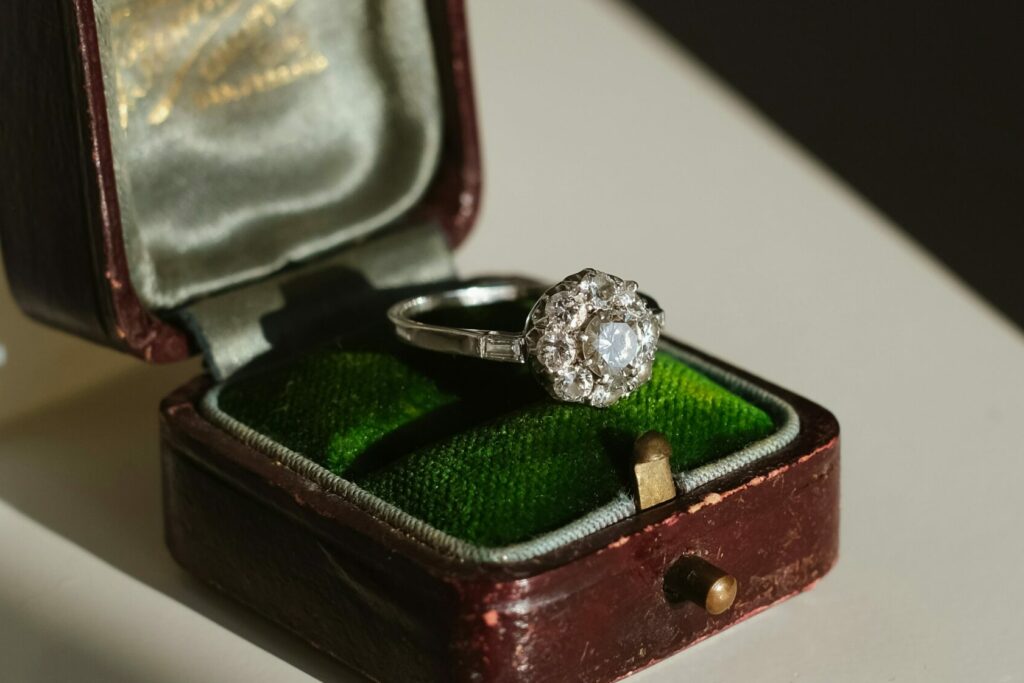A vintage engagement ring with 7 diamonds resting on a velvet-lined antique ring box